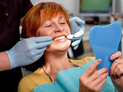 The image shows a woman sitting in a dental chair, receiving a teeth cleaning from a dentist.