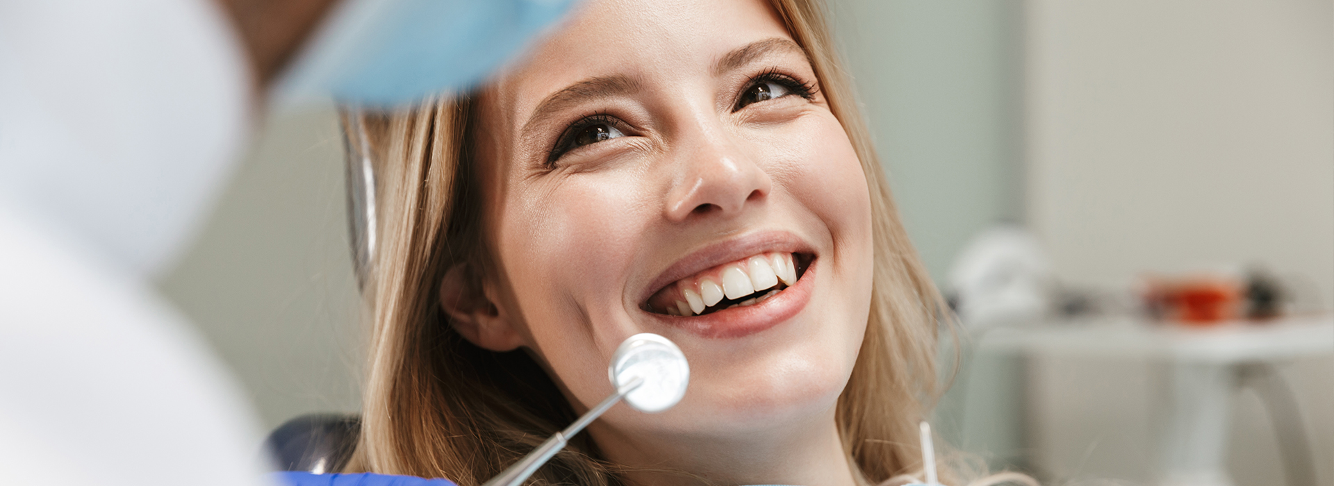 The image shows a woman sitting in front of a dental chair, with a dentist and dental equipment in the background.